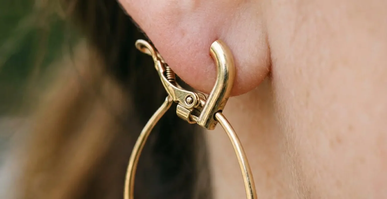 Gros plan sur le mécanisme de fermeture d'une boucle d'oreille dormeuse en or, illustrant la sécurité du système pour les sportives