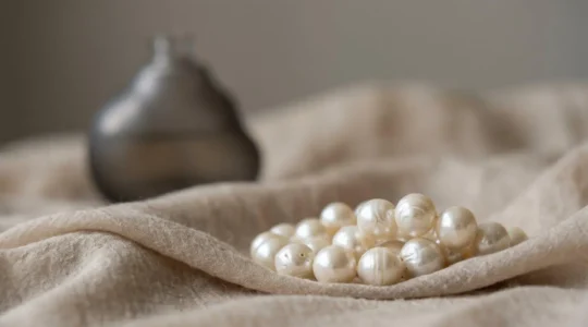 Gros plan artistique de perles de culture nacrées avec reflets naturels et flacon de parfum en arrière-plan flou